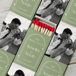 May include: Matchboxes with a green background and the text "The Perfect Match" with the names "Amelia & Noah" and the date "07.14.2027". The matchboxes contain matches with red tips. A black and white photo of a couple is on the matchbox.