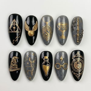 May include: A set of ten almond-shaped press-on nails featuring black and grey marble backgrounds with raised gold metallic designs including a deathly hallows symbol, a golden snitch, a letter S pendant, a goblet, a wand, a hat, a stag, a potion bottle, glasses with a lightning bolt, and a time turner.