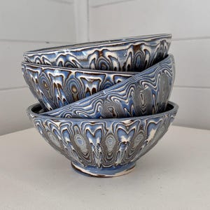 May include: A set of three ceramic mugs with a speckled, matte finish. The mugs are in shades of cream, light gray, and dark gray. Each mug has a simple, minimalist design, perfect for coffee or tea.