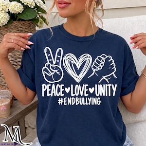 May include: A navy blue t-shirt featuring a white graphic design with a peace sign, a scribbled heart, and two hands clasped together. Below the graphic, the text reads PEACE LOVE UNITY and #ENDBULLYING in a bold, white sans-serif font.