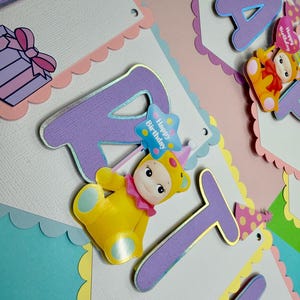 May include: A colorful birthday banner with the word "PARTY" spelled out in large, lavender letters with gold trim. The banner features a scalloped edge and is decorated with cartoon figures and the words "Happy Birthday".