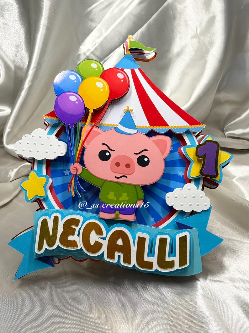 Puede incluir: Un adorno para tarta de papel multicapa que presenta un cerdo de dibujos animados con un sombrero de fiesta azul y una camisa verde, sosteniendo un racimo de globos de colores. El dise&ntilde;o incluye una carpa de circo a rayas rojas y blancas, nubes blancas, una estrella amarilla, un n&uacute;mero 1 morado y una pancarta azul con el nombre NECALLI en letras doradas.