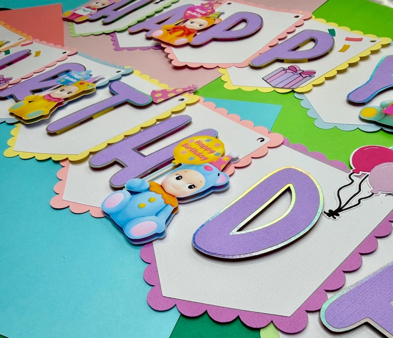 May include: A colorful birthday banner with the words "HAPPY BIRTHDAY" in purple letters. Each letter is on a white scalloped edge card. The banner includes cartoon baby figures and balloons. The background is a mix of pastel colors.