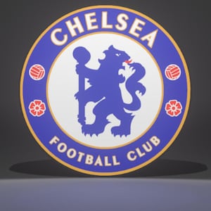 May include: A circular emblem featuring the words "CHELSEA FOOTBALL CLUB" in white lettering on a blue background. The emblem includes a blue lion holding a staff, surrounded by red and white soccer balls and floral designs.