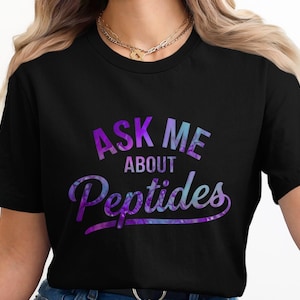 May include: Black t-shirt with the text "ASK ME ABOUT Peptides" in a tie-dye style design. The text is in shades of purple and blue. The shirt is a crew neck and short-sleeved.