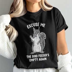 May include: Black crew neck t-shirt featuring a squirrel illustration. The text on the shirt says "EXCUSE ME THE BIRD FEEDER'S EMPTY AGAIN". The graphic is in white.