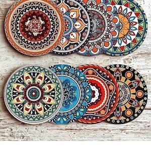 May include: Eight circular coasters with detailed mandala patterns in various colours, including orange, blue, green, and red. The coasters are arranged in two rows of four, displaying their decorative designs. Each coaster has a diameter of approximately 10 cm.