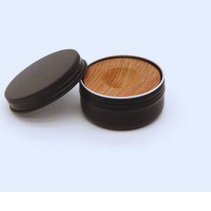 Könnte beinhalten: Ein kleiner, runder, dunkelbrauner Behälter mit passendem Deckel. Der Behälter ist geöffnet und zeigt einen Einsatz aus Birnenholz. Der Text "PEAR WOOD" ist oben im Bild in Schwarz gedruckt.