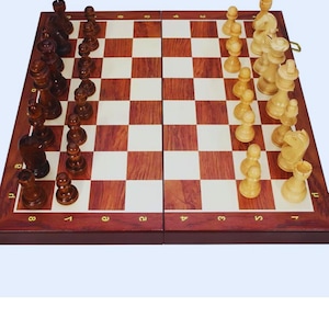 Puede incluir: Un juego de ajedrez de madera con cuadrados de color marrón oscuro y madera clara. Las piezas de ajedrez están dispuestas en el tablero, con piezas de color marrón oscuro en un lado y piezas de madera clara en el otro. El tablero está enmarcado en madera marrón oscuro.