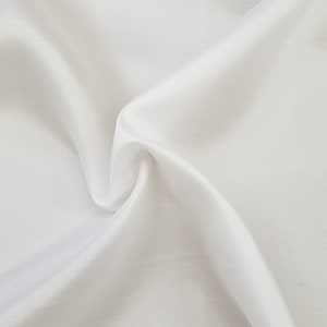 May include: White fabric with soft folds and wrinkles. The fabric is smooth and silky.