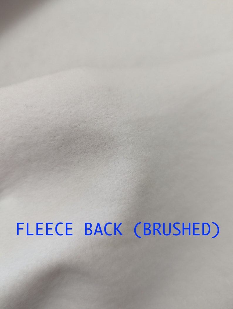 Pu&ograve; includere: Primo piano di un tessuto bianco con una texture morbida e spazzolata. Il testo "FLEECE BACK (BRUSHED)" &egrave; stampato sul tessuto.
