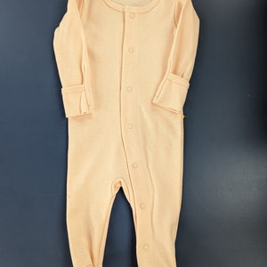 May include: A peach-colored baby onesie with long sleeves and snap buttons down the front.
