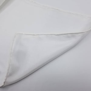 Pode incluir: Um quadrado de tecido branco com uma borda dobrada. O tecido &eacute; liso e tem um brilho sutil.