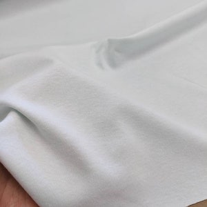 May include: A light blue fabric with a smooth texture. The fabric is folded and draped over a hand.