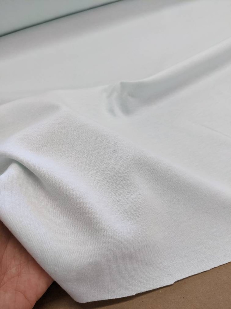 May include: A light blue fabric with a smooth texture. The fabric is folded and draped over a hand.