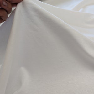 May include: White cotton fabric with a smooth texture. The fabric is folded and draped over a surface.
