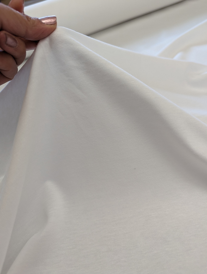 May include: White cotton fabric with a smooth texture. The fabric is folded and draped over a surface.
