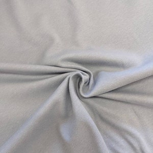 May include: A close-up of a light gray fabric with a smooth texture. The fabric is folded and draped, showing its soft and drapey quality.