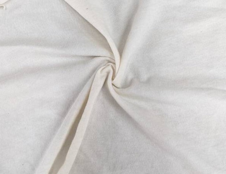 Puede incluir: Primer plano de una tela blanca texturizada con un tacto suave y liso. La tela est&aacute; doblada y drapeada, mostrando su textura natural.