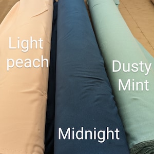 May include: Three rolls of fabric in different colors: light peach, midnight blue, and dusty mint. The fabric rolls are lying on a light brown surface.