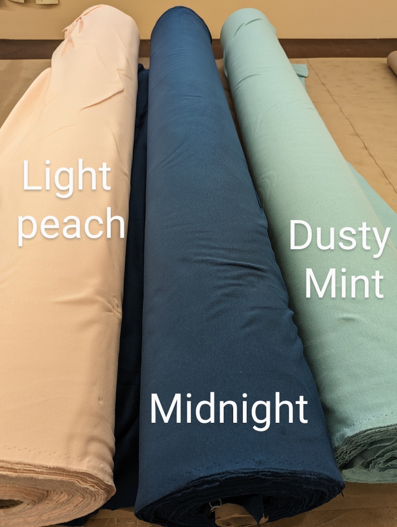 May include: Three rolls of fabric in different colors: light peach, midnight blue, and dusty mint. The fabric rolls are lying on a light brown surface.