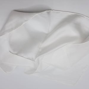 Pode incluir: Um len&ccedil;o de seda branco, dobrado e drapeado, mostrando sua textura lisa e seu drapeado delicado.