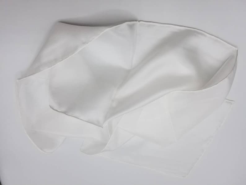 Pode incluir: Um len&ccedil;o de seda branco, dobrado e drapeado, mostrando sua textura lisa e seu drapeado delicado.