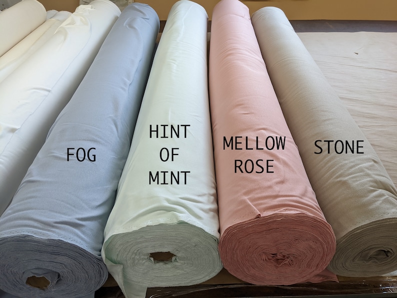 May include: Five rolls of fabric in different colors: light blue, light green, light pink, and beige. The fabric rolls are labeled "Fog", "Hint of Mint", "Mellow Rose", and "Stone".