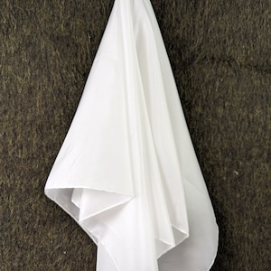 Pode incluir: Um len&ccedil;o de tecido branco e transparente pendurado em um fundo marrom texturizado.