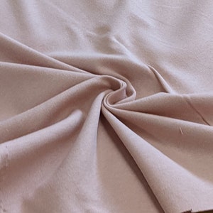 May include: A close-up of a soft, pale pink fabric with a smooth texture. The fabric is folded and draped, showing its natural drape and flow.