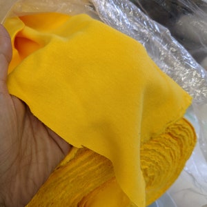 May include: A bright yellow fabric roll, folded and partially unrolled, is held in a clear plastic bag.