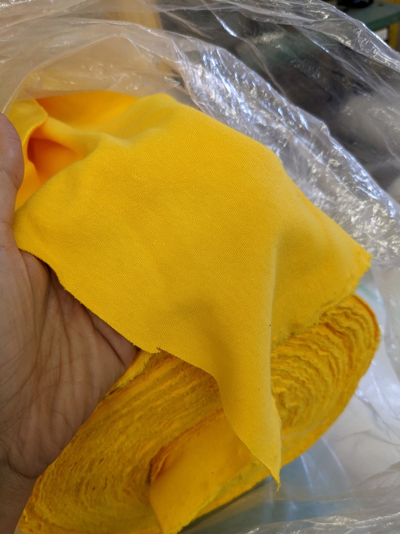 May include: A bright yellow fabric roll, folded and partially unrolled, is held in a clear plastic bag.