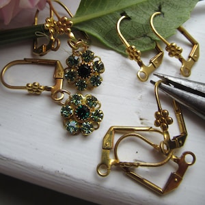 May include: Gold earring findings with green crystal flower accents. The findings are in various shapes and sizes, including a teardrop, a circle, and a square.