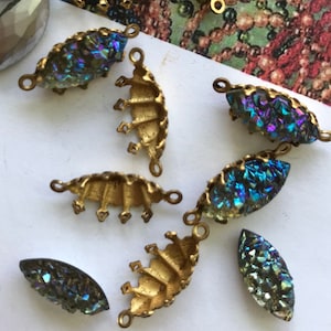 May include: A collection of vintage jewelry components, including iridescent druzy stones and gold-toned metal findings. The components are in various shapes, including teardrops and fan-like designs. The background features a vintage magazine illustration.