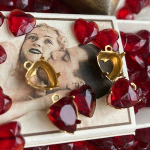 May include: A vintage matchbox filled with red glass heart-shaped embellishments.  The box is open and there are several gold heart-shaped metal findings with loops on top.