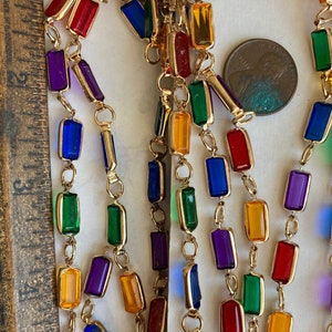 Puede incluir: Una cadena de oro con cuentas de vidrio rectangulares de colores. Las cuentas son en tonos de rojo, naranja, amarillo, verde, azul y morado.