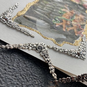 May include: A white card with a gold glitter border and a picture of two cherubs inside. The card is decorated with silver floral embellishments around the edges.