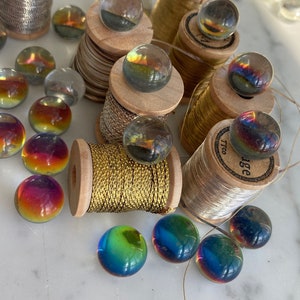Peut inclure: Une collection de billes en verre color&eacute;es sur des bobines de fil d'or et d'argent. Les billes sont iris&eacute;es et ont un effet arc-en-ciel. Les bobines sont en bois et ont un aspect vintage.