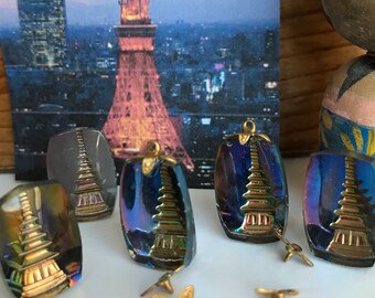 May include: Five iridescent glass pendants with gold accents featuring a pagoda design. The pendants are arranged on a white surface with gold metal jump rings and earring backs.