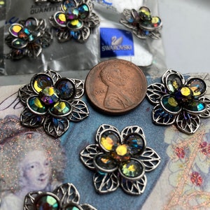 May include: A close-up of seven silver flower-shaped embellishments with iridescent rhinestones. The embellishments are scattered on a surface with a vintage design. A penny from 1986 is in the center of the image.