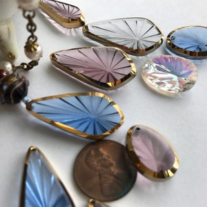 May include: Assortment of eight teardrop-shaped crystal pendants with gold trim. The pendants are in shades of blue, purple, and clear.
