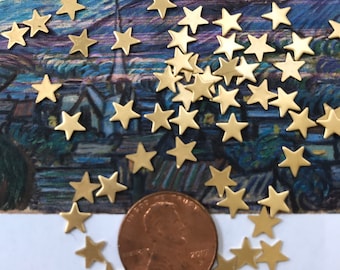 以下が含まれることがあります： 金色の金属製の星形のチャームが散らばっており、いくつかはアメリカの1セント硬貨の周りに円形に配置されています。