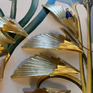 May include: Five gold-colored metal fan-shaped ornaments with a textured surface. The ornaments are arranged in a fan shape on a white surface.