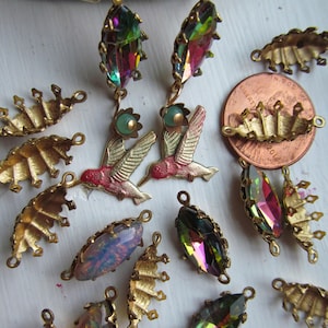 May include: A collection of vintage jewelry components, including iridescent crystal pendants, hummingbird charms, and gold-toned leaf-shaped findings. The crystals display a rainbow of colors. A U.S. penny is included for size reference.