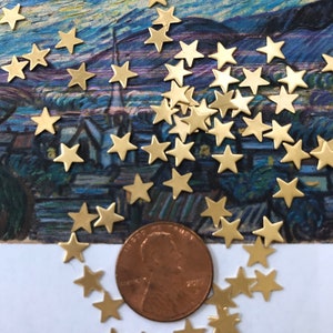 Puede incluir: Una dispersión de abalorios de metal de color dorado en forma de estrella, algunos dispuestos en círculo alrededor de un centavo estadounidense.