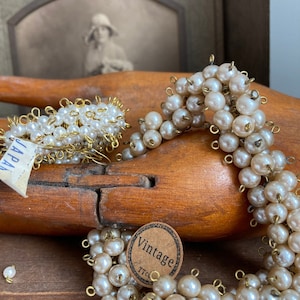 Puede incluir: Dos collares vintage de perlas con alambre dorado y bucles. Los collares están sobre una superficie de madera con una etiqueta que dice "Vintage".