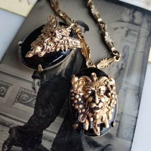 May include: A gold chain necklace with two black cameo pendants featuring detailed gold sculpted faces with foliage accents.
