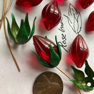 Puede incluir: Brotes de rosa de vidrio rojo con hojas verdes, algunos con tallos de alambre dorado, y un centavo estadounidense para la escala.