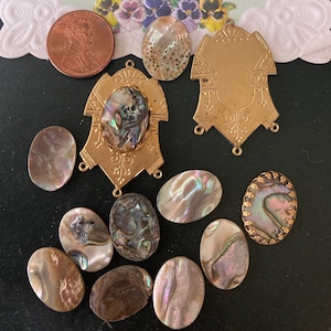 May include: A collection of iridescent abalone shell pieces and gold-toned metal findings. The shells vary in size and color, with hues of pink, green, and purple. A U.S. penny is included for size reference. The metal pieces have decorative designs.