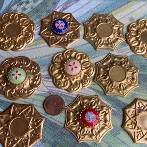May include: Assortment of ten gold-toned metal decorative embellishments with intricate floral designs. Each embellishment features a center circle with a painted floral design in various colors, including red, blue, green, and white.